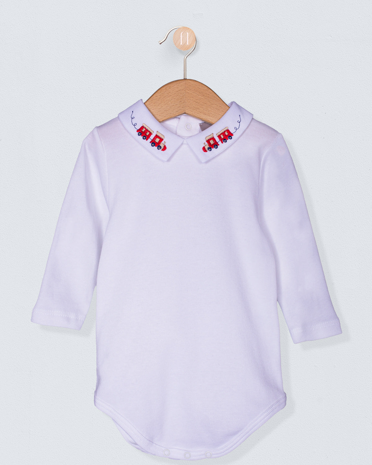 White baby shirt with embroidered train on collar on a hanger against a light gray background