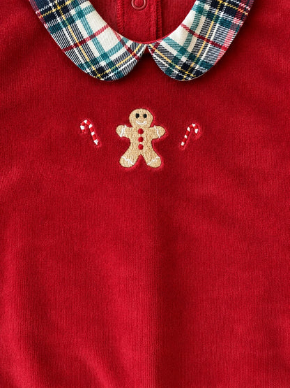 Close-up of a red knit garment with a plaid collar in blue, green, white, and yellow, featuring an embroidered gingerbread man and candy canes on the chest.