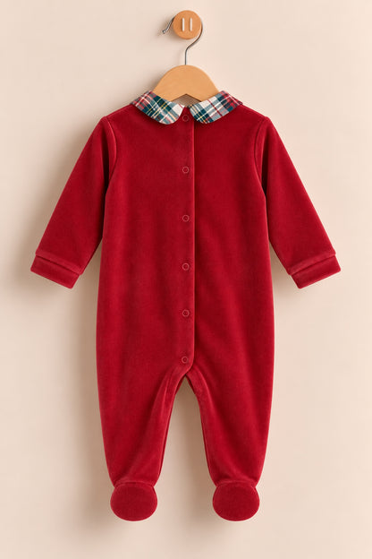 A baby's red footed sleeper with a plaid collar, hanging on a wooden hanger against a light beige background.