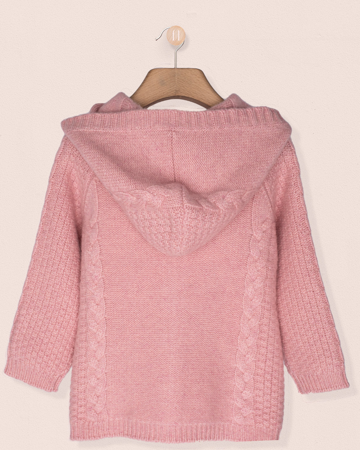 Back of a pink cashmere knitted jacket on a hanger against a light pink background
