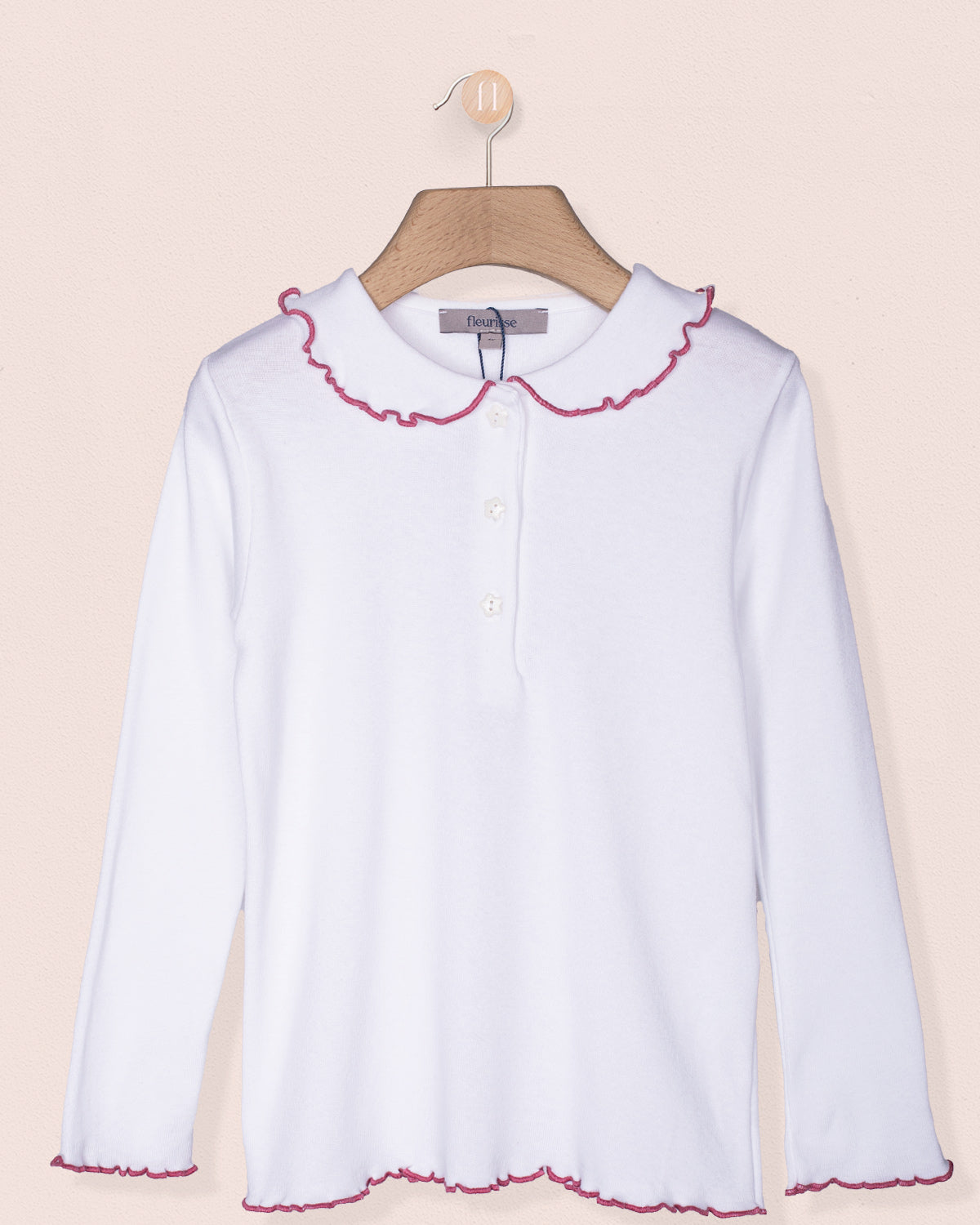 White blouse with pink trim on a hanger against a beige background