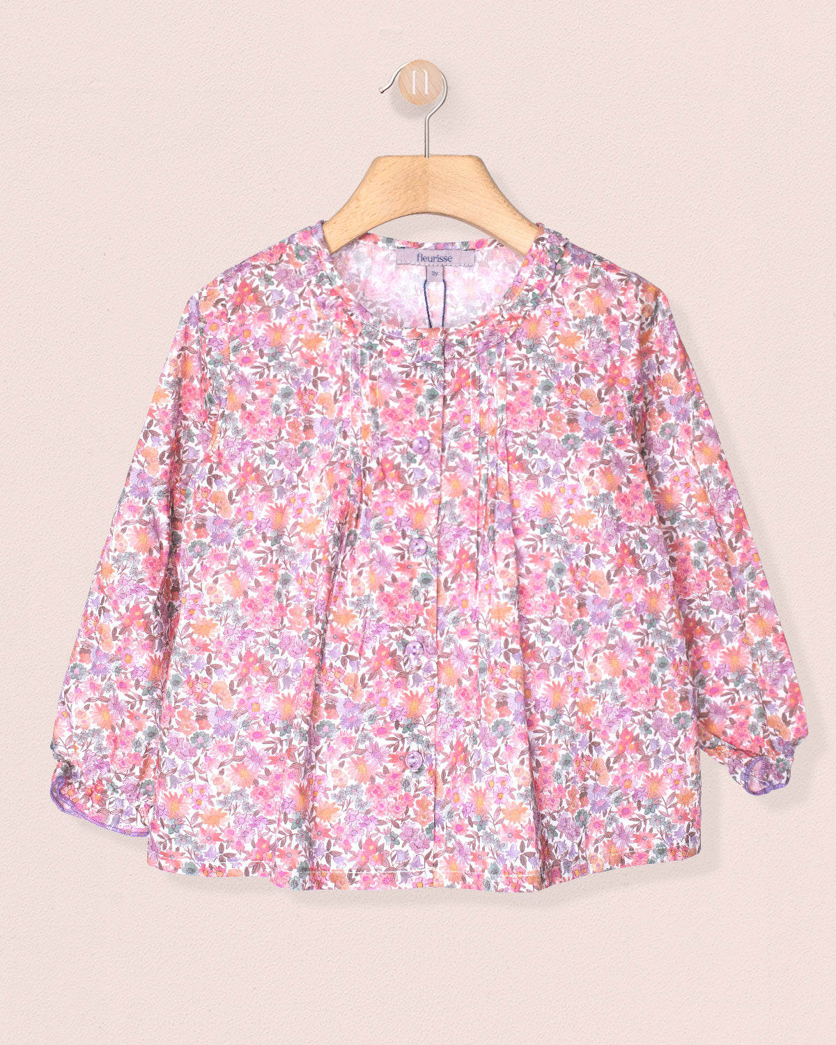 Floral patterned blouse on a hanger against a beige background