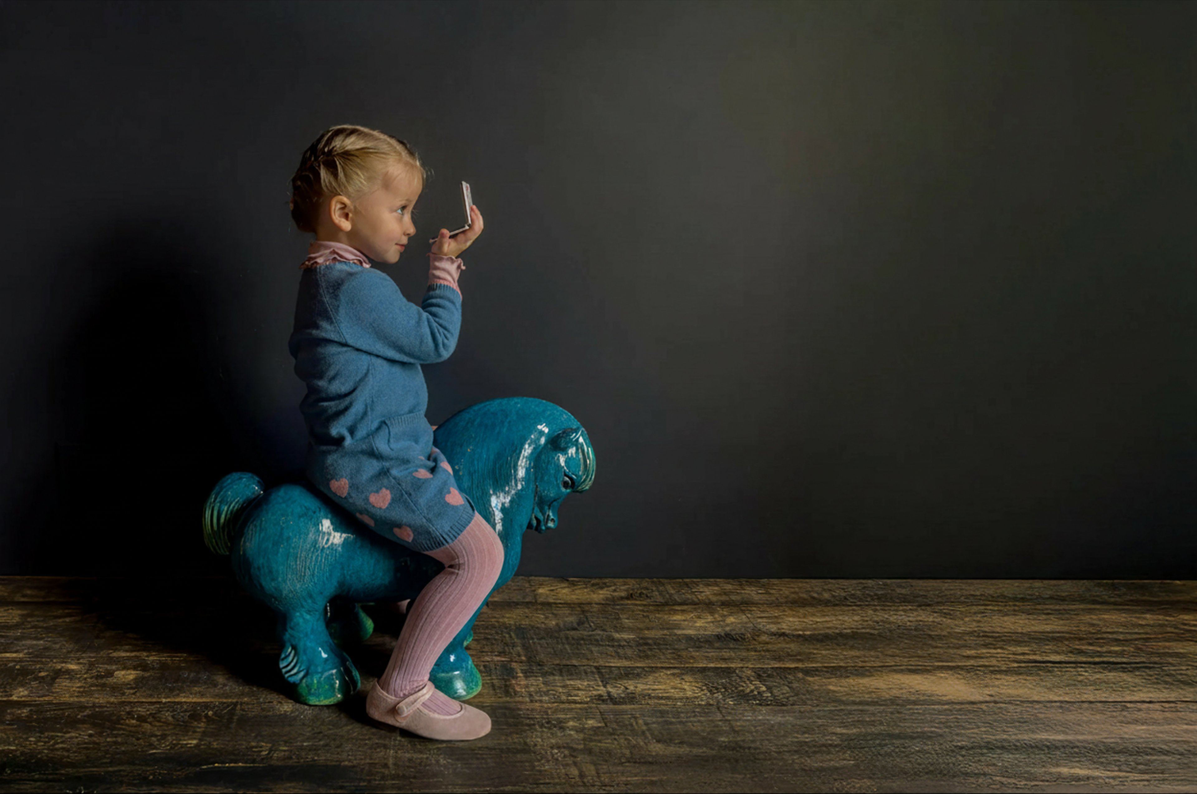 Child sitting on a blue toy horse against a dark background