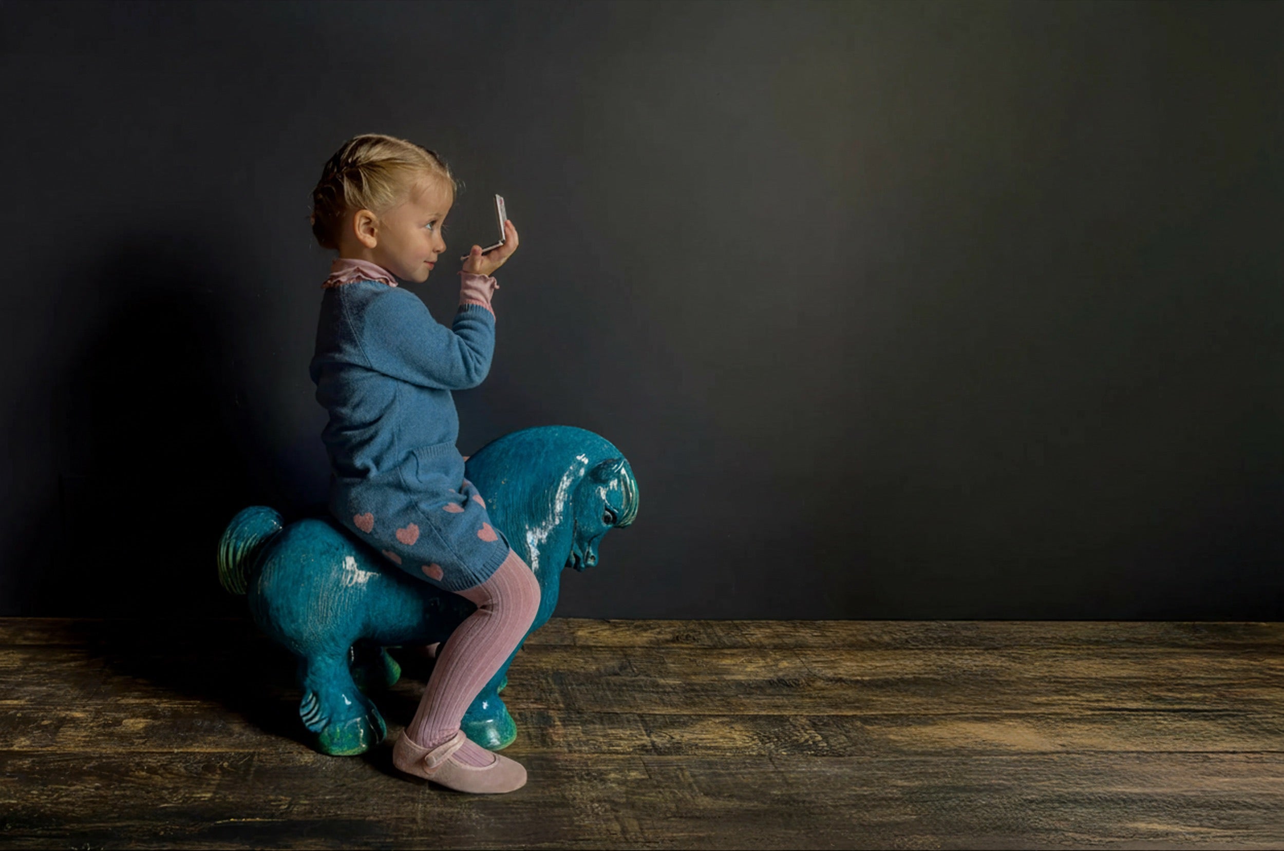 Child sitting on a blue horse toy against a dark background