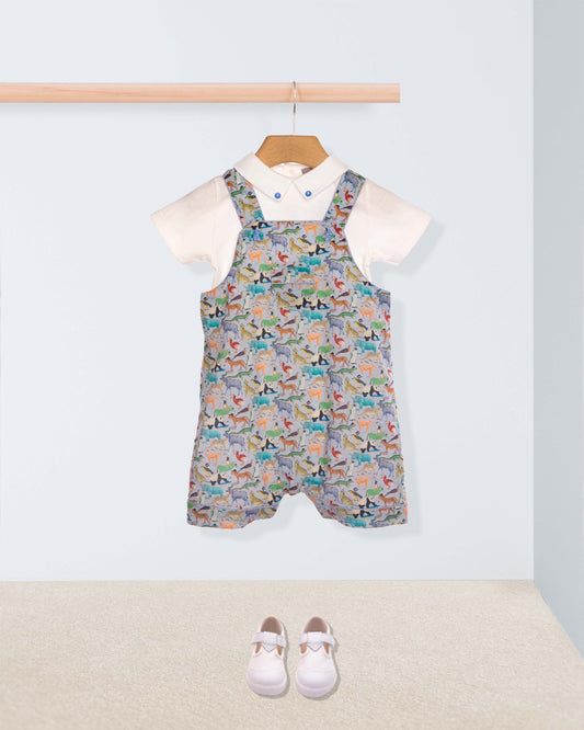 Children's patterned overalls hanging on a rack with white shoes on the floor.