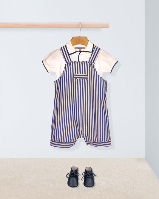 Children's outfit with striped overalls and navy shoes on a plain background