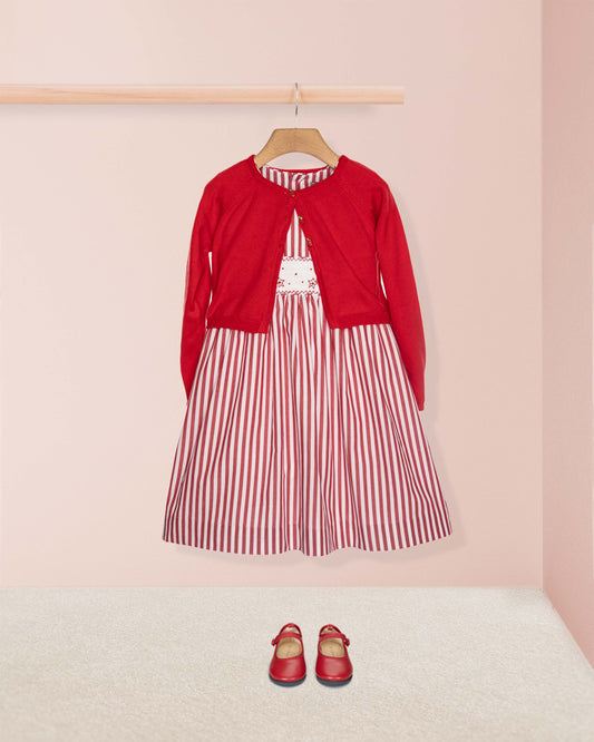 Red cardigan over a red and white striped dress with matching shoes on a pink background