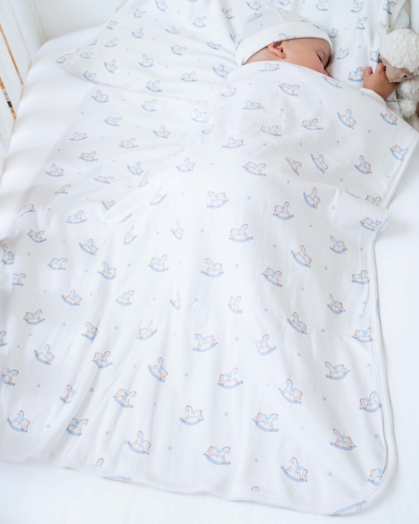 Baby model sleeping in a crib- wrapped in Pima Blue Rocking Horse Blanket