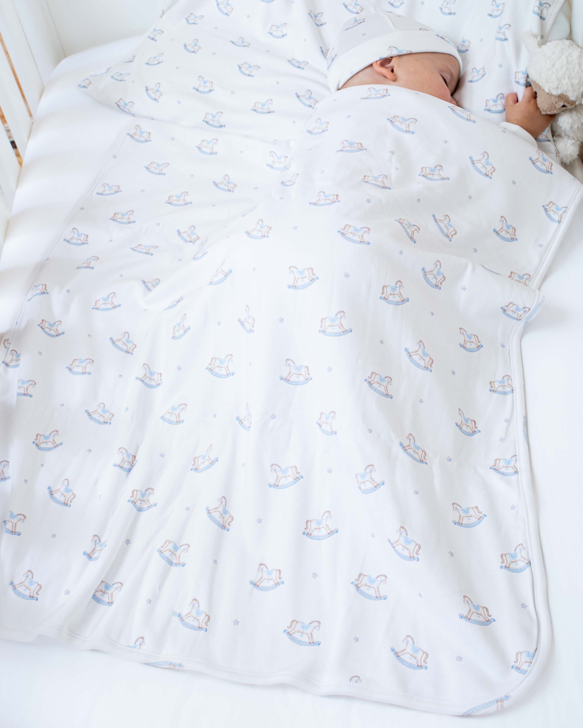 Baby model sleeping in a crib- wrapped in Pima Blue Rocking Horse Blanket