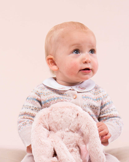 Baby model wearing Courchevel Cashmere Pink Cardigan sitting down with a bunny toy, wearing a coordinating embroidered collared onesie showing the details of the sweater 