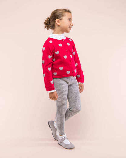 Girl model wearing Madeleine Red Hearts Cashmere sweater facing to the front looking to the side showing the front details of the sweater; paired with leggings and shoes in contrasting grey color and a white turtleneck