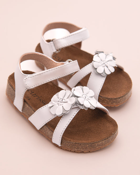 White leather toddler sandals with cork footbed and white flower details, displayed at an angle as a pair.