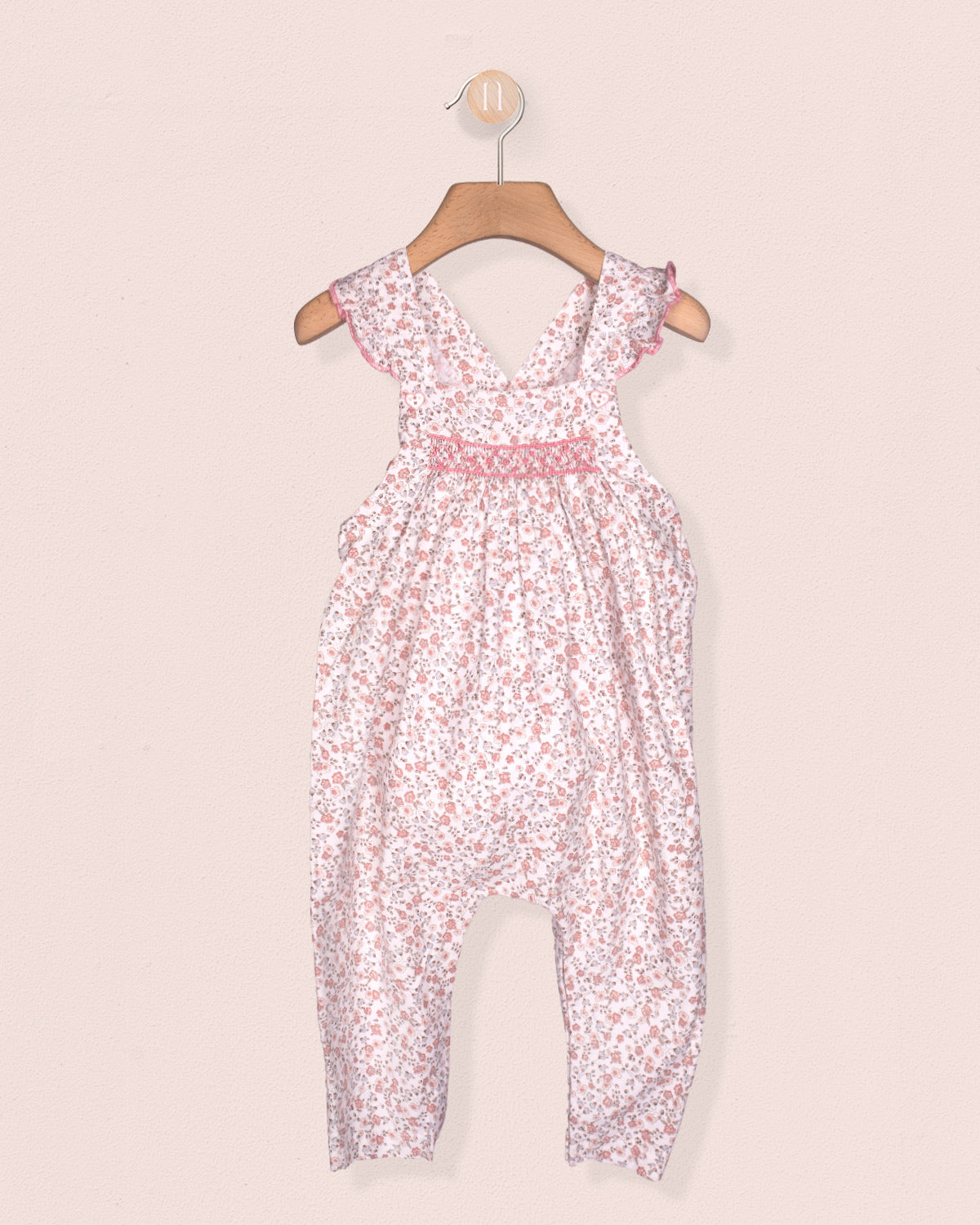 Floral-patterned jumpsuit on a hanger against a light pink background