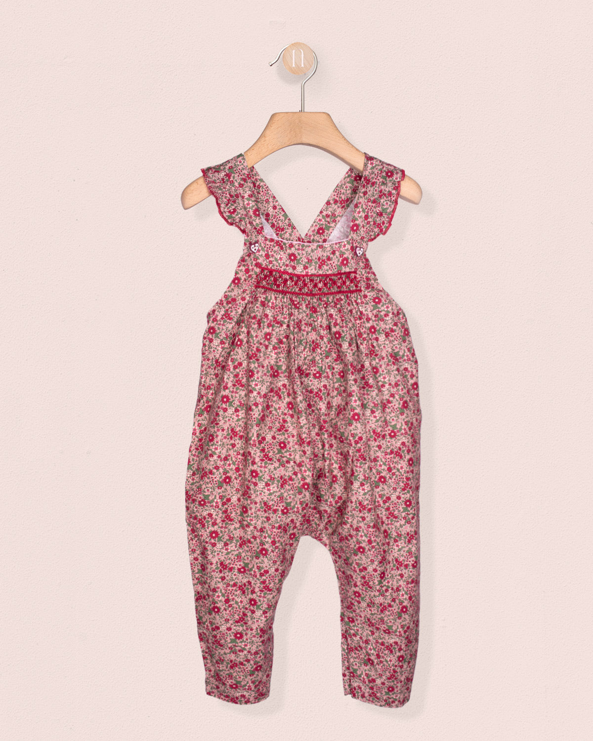 Floral-patterned jumpsuit on a hanger against a light pink background