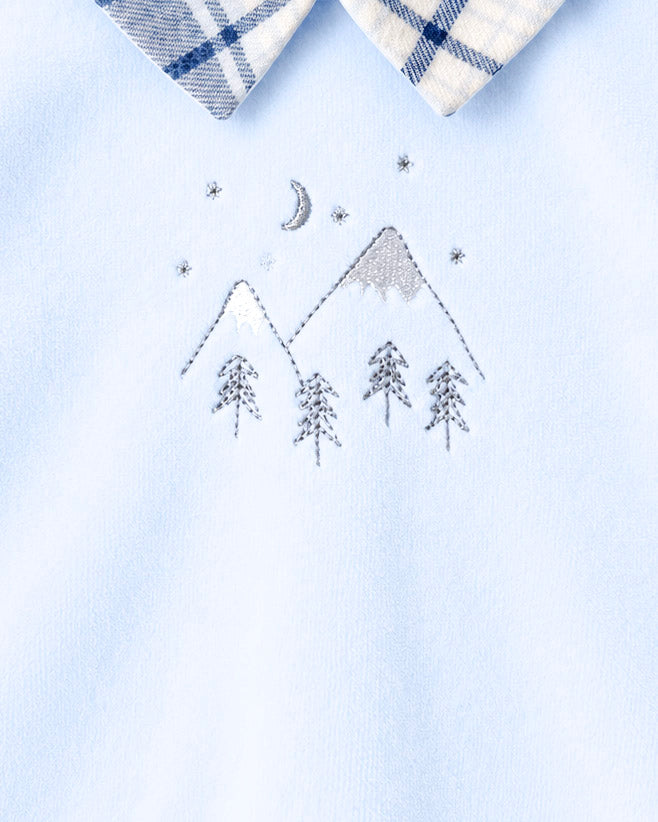 Close-up of a light blue garment with a white and navy plaid collar and an embroidered mountain, moon, stars, and trees motif on the chest.