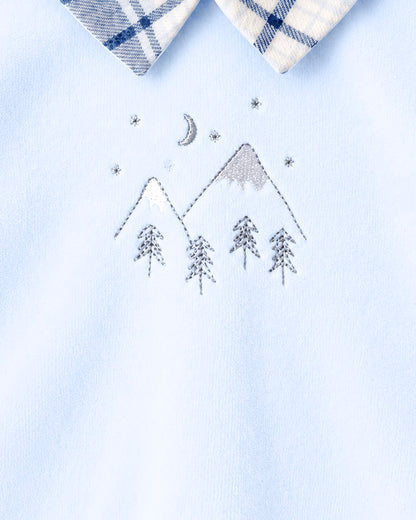 Close-up of a light blue garment with a white and navy plaid collar and an embroidered mountain, moon, stars, and trees motif on the chest.