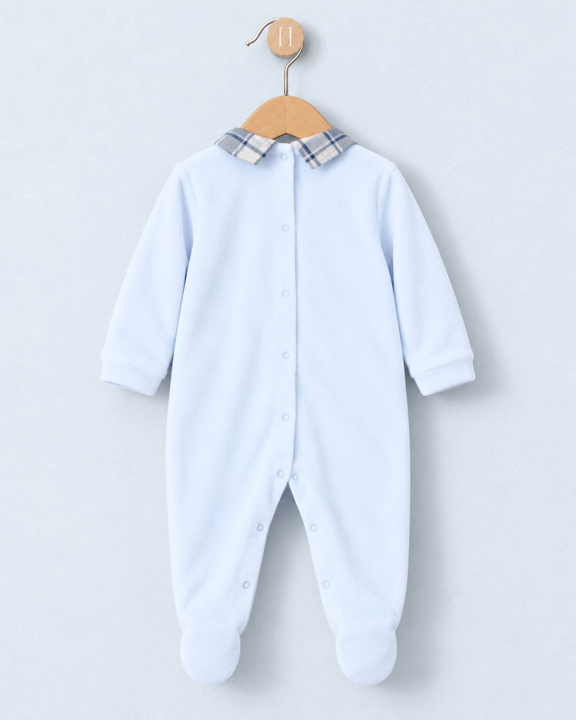 A baby long-sleeve footed sleeper in light blue, featuring a plaid collar and snap-button front, hanging on a wooden hanger against a light gray background.