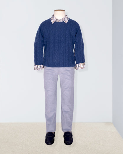 Mannequin wearing a blue cable knit sweater with patterned collar and cuffs, gray pants, and navyshoes on a light gray background.