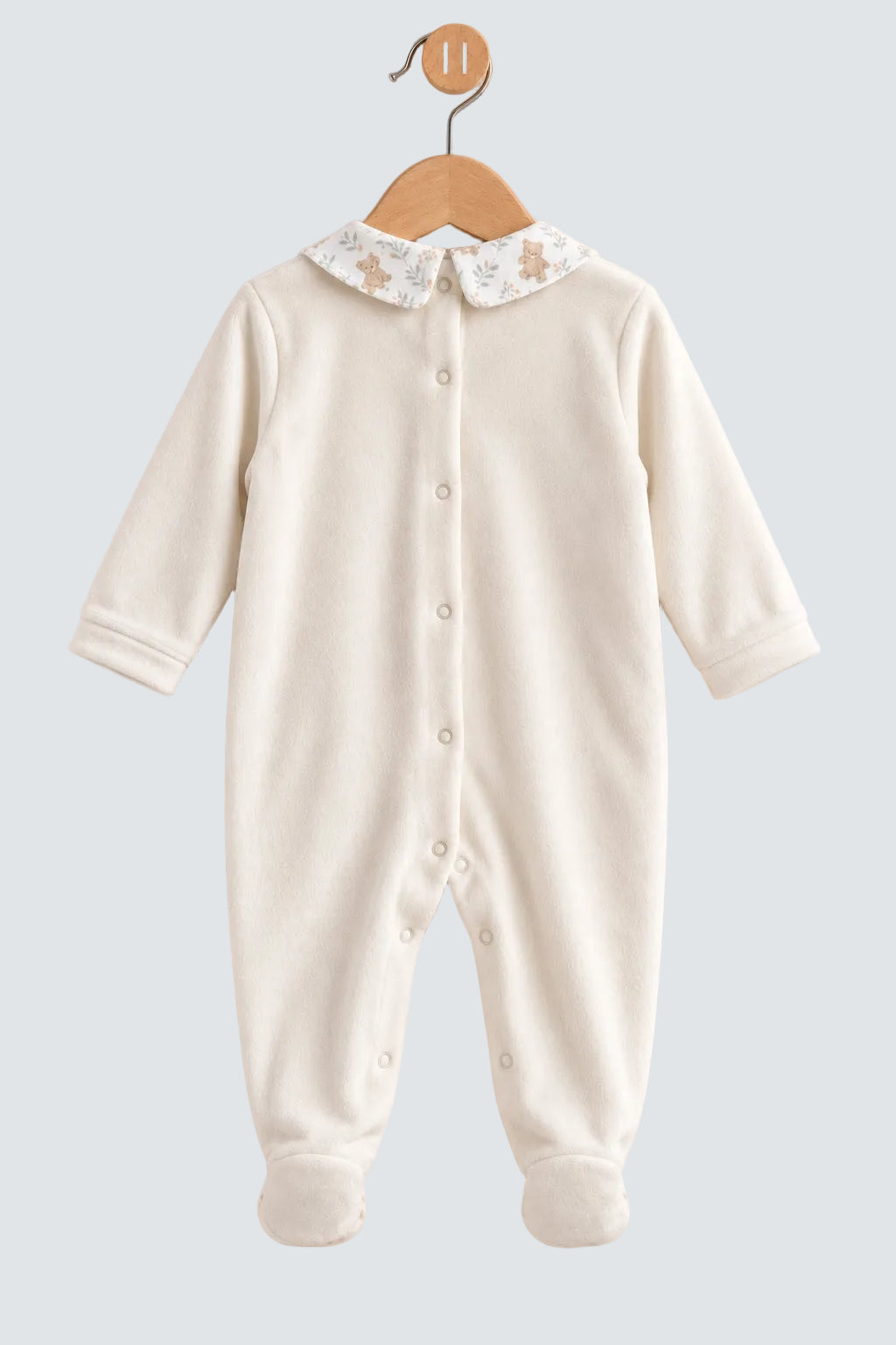 An off-white long-sleeve baby footed sleeper with a decorative floral and star-patterned Peter Pan collar, hanging on a wooden hanger against a soft beige background.