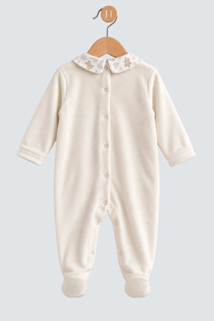 An off-white long-sleeve baby footed sleeper with a decorative floral and star-patterned Peter Pan collar, hanging on a wooden hanger against a soft beige background.