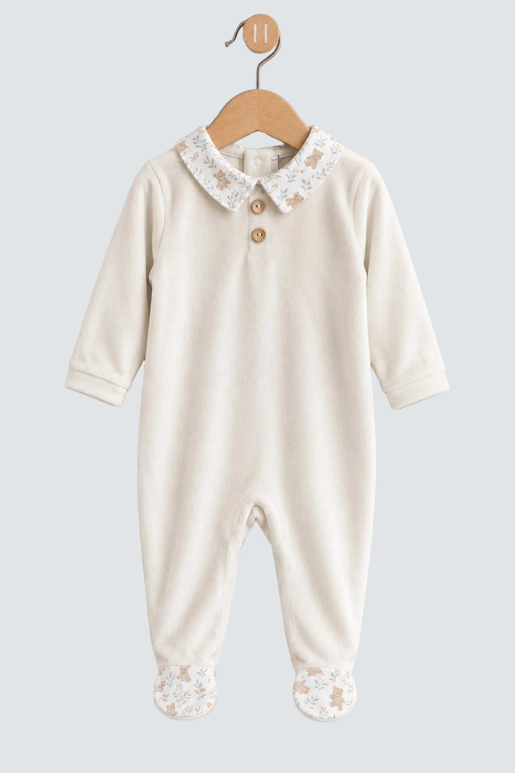 An off-white baby footed jumpsuit with a lace Peter Pan collar and decorative buttons, hanging on a wooden hanger against a light gray background.