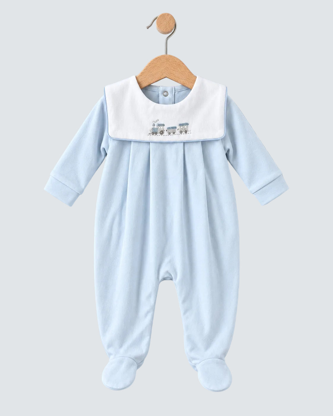 A baby footed sleeper in light blue with a contrasting white bib collar featuring a small embroidered train design, hanging on a wooden hanger against a light blue background.
