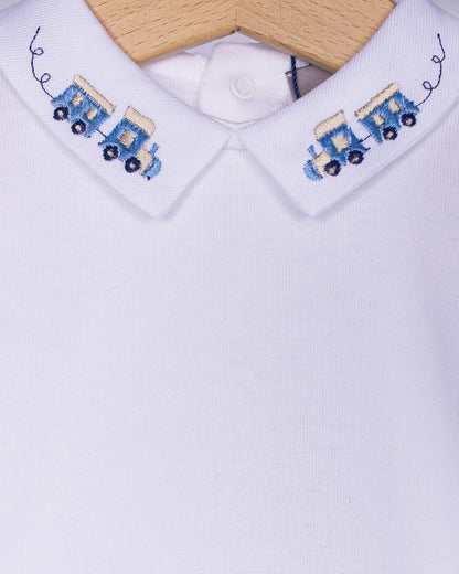 Close-up 
White shirt with embroidered blue train designs on collar and cuffs, on a wooden hanger.