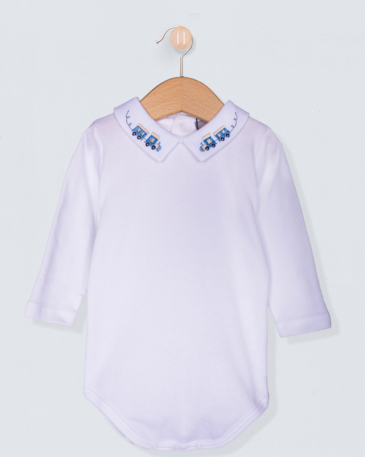 White baby shirt with embroidered collar on a wooden hanger against a light gray background