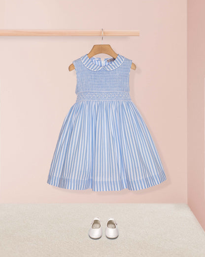 Blue and white striped dress on a hanger against a pink wall with white shoes on the floor.