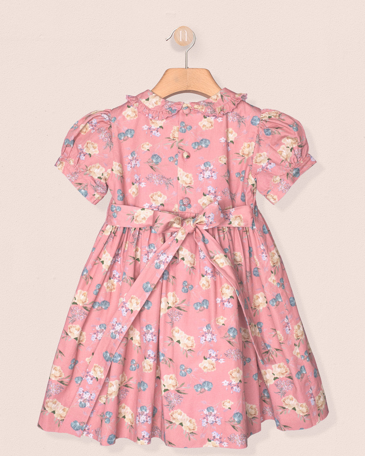 Pink floral dress on a hanger against a beige background