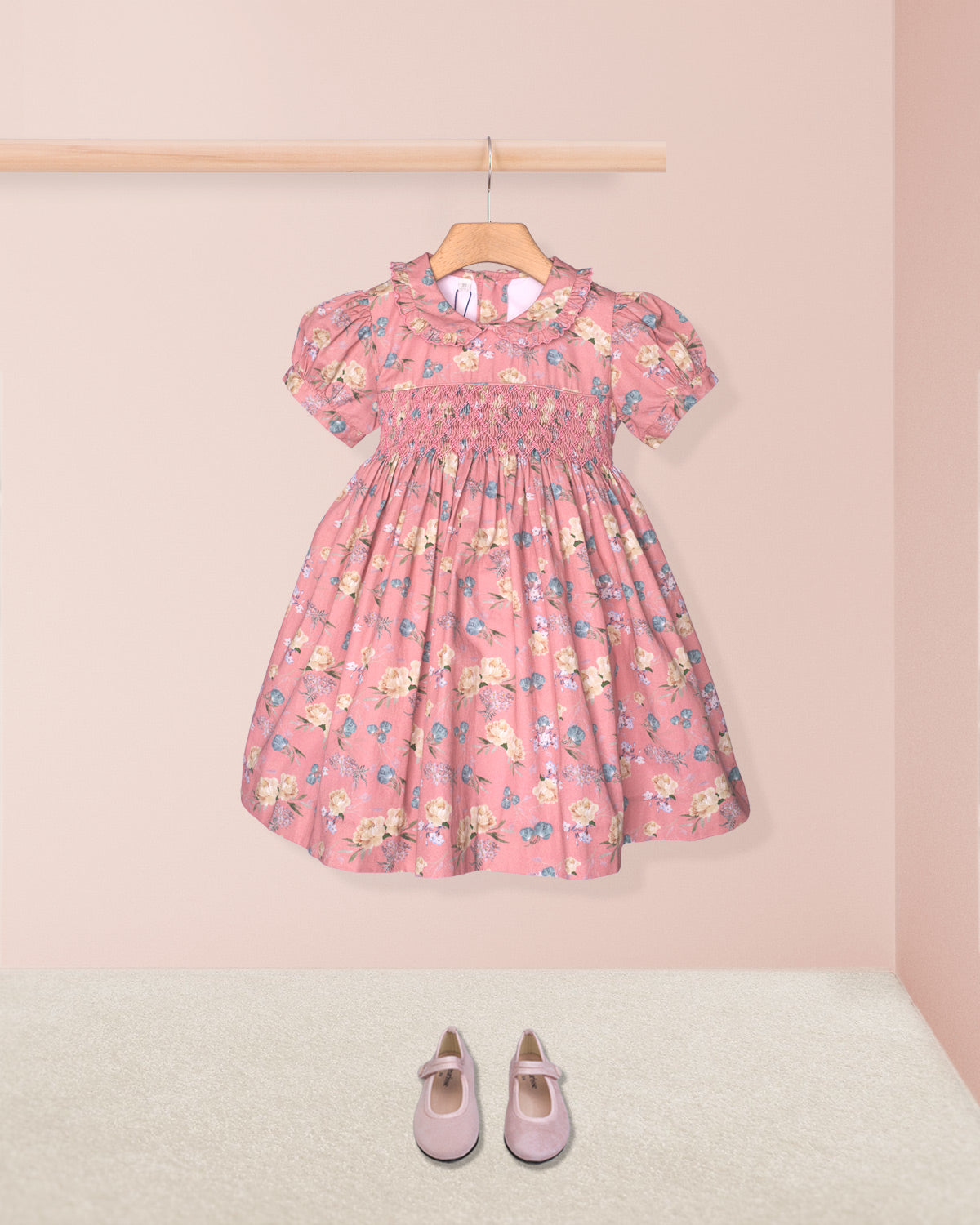 Pink floral dress on a hanger with matching shoes on the floor against a pink background