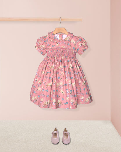 Pink floral dress on a hanger with matching shoes on the floor against a pink background