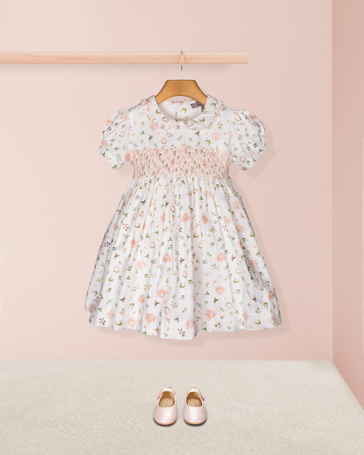 Styled flat-lay of the Valentina Soft Pink Toscana Smocked Dress with matching blush Mary Jane shoes beneath, set against a neutral pink and beige backdrop for a complete look.