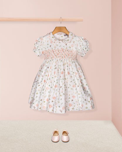 Styled flat-lay of the Valentina Soft Pink Toscana Smocked Dress with matching blush Mary Jane shoes beneath, set against a neutral pink and beige backdrop for a complete look.