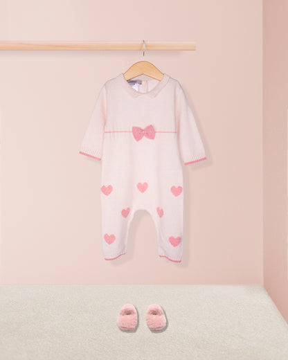 Baby onesie with heart patterns and matching shoes on a pink background