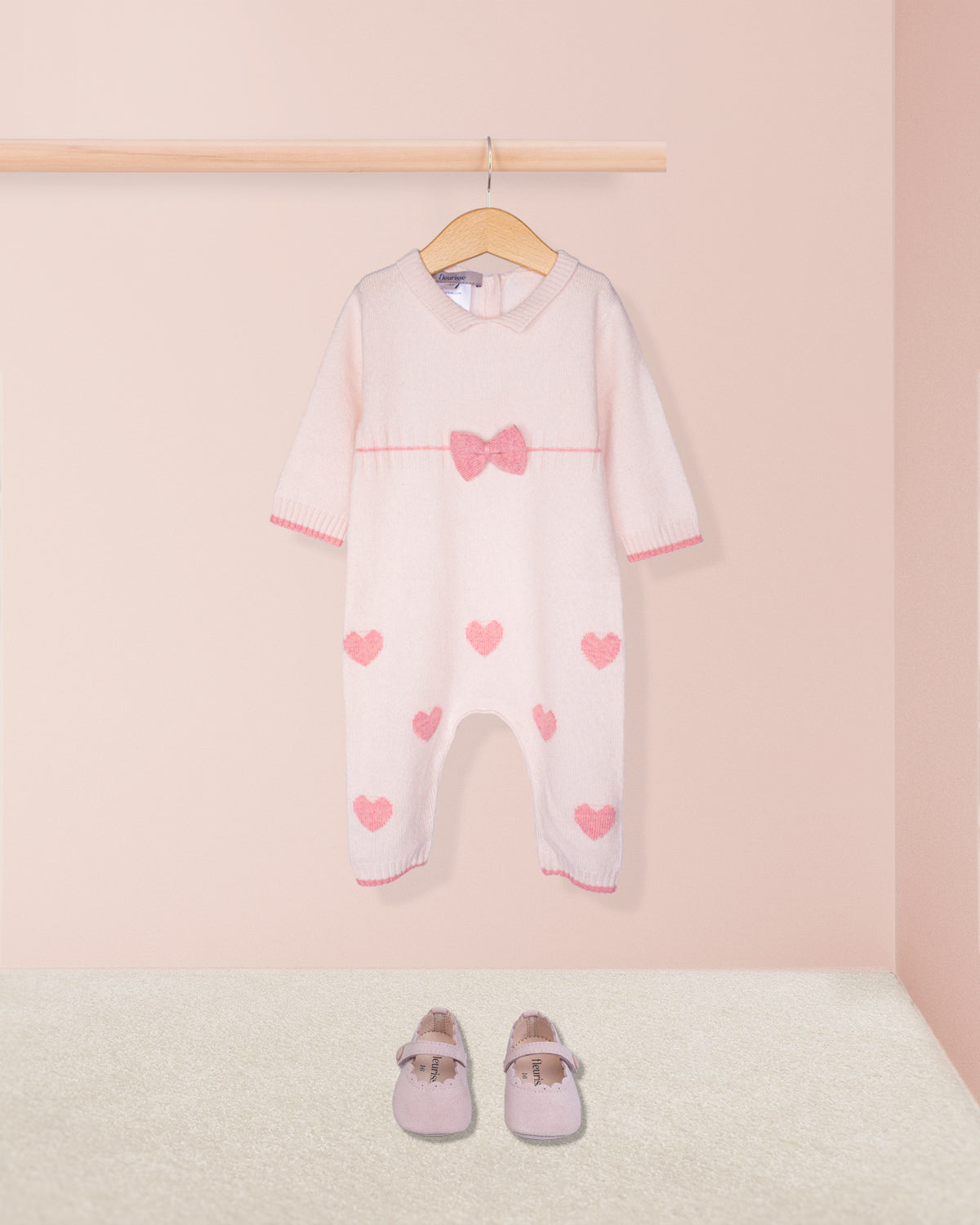Baby onesie with heart patterns on a hanger against a pink background