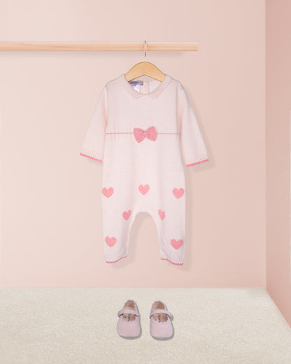 Baby onesie with heart patterns on a hanger against a pink background