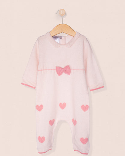 Front of cashmere baby onesie with pink hearts and a bow on a hanger against a light background
