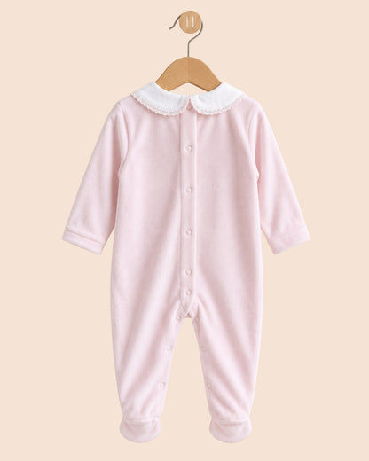 A light pink long-sleeve baby footed jumpsuit with a white Peter Pan collar, hanging on a wooden hanger against a solid beige background.