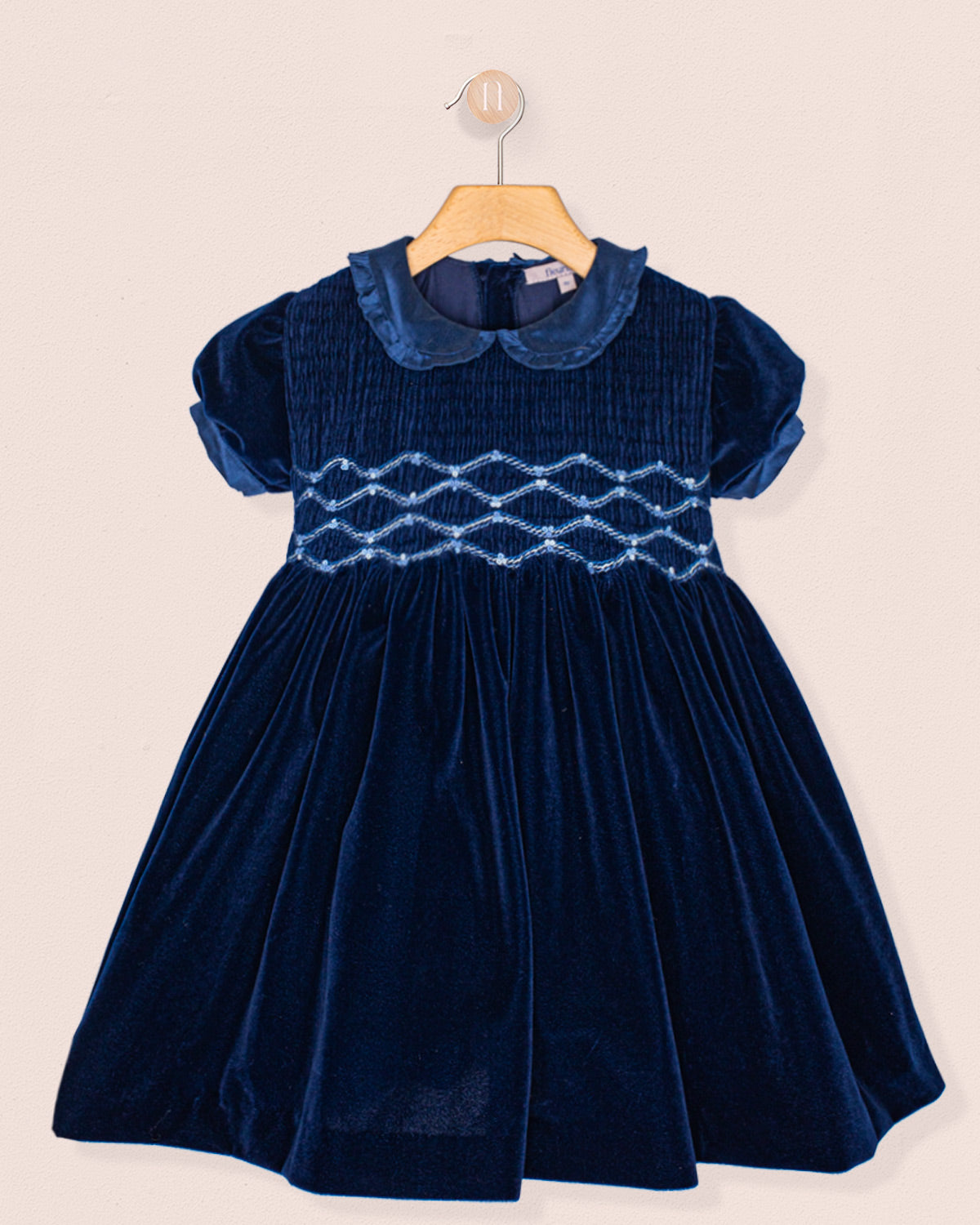 Navy blue velvet dress with a textured smock on a beige background