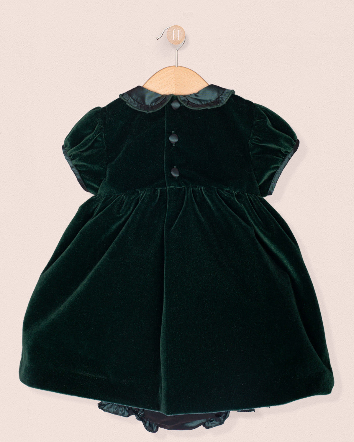 Green velvet dress on a hanger against a beige background