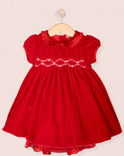 Red dress with smocked bodice on a hanger against a beige background