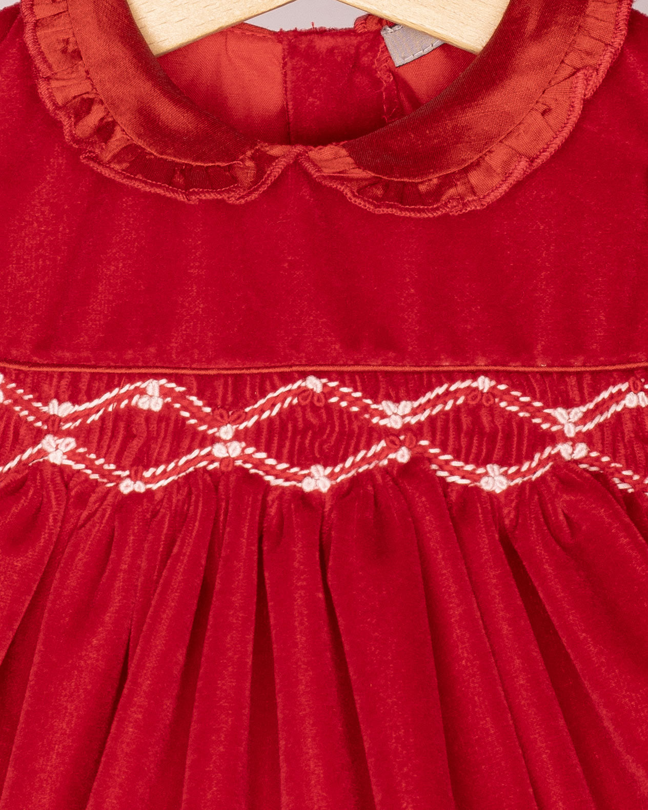 Red velvet dress with smocked details on a hanger