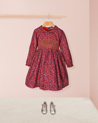 Children's floral dress on a hanger with shoes on the floor against a pink background