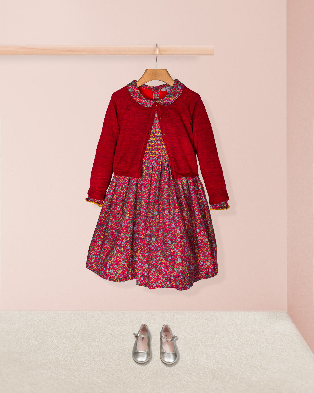Red cardigan over a floral dress with silver shoes on a pink background
