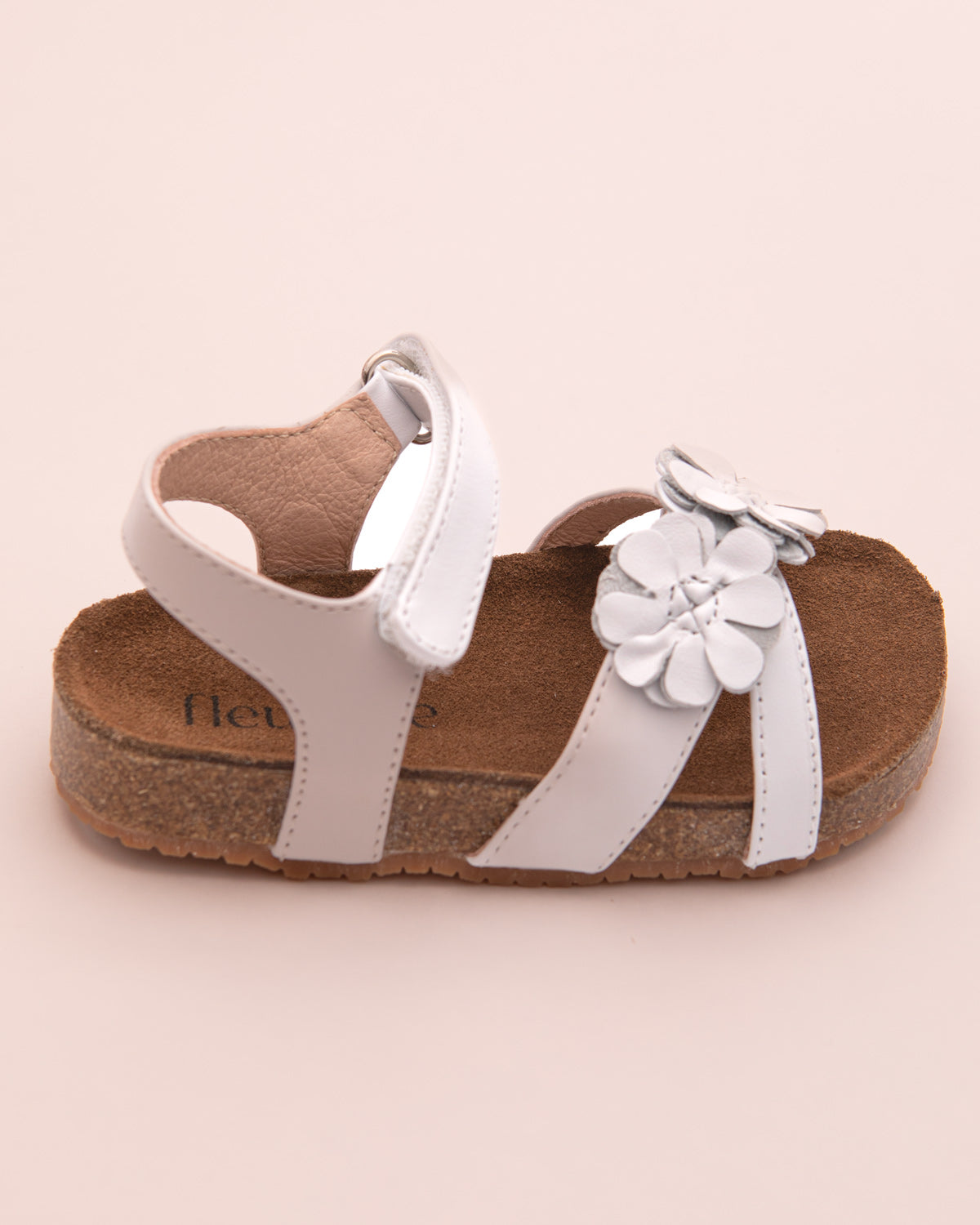Side profile of a white leather toddler sandal with floral appliqué and adjustable ankle velcro strap.