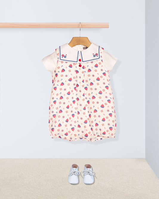 Children's romper with collar hanging on a rack, accompanied by baby shoes on the floor.