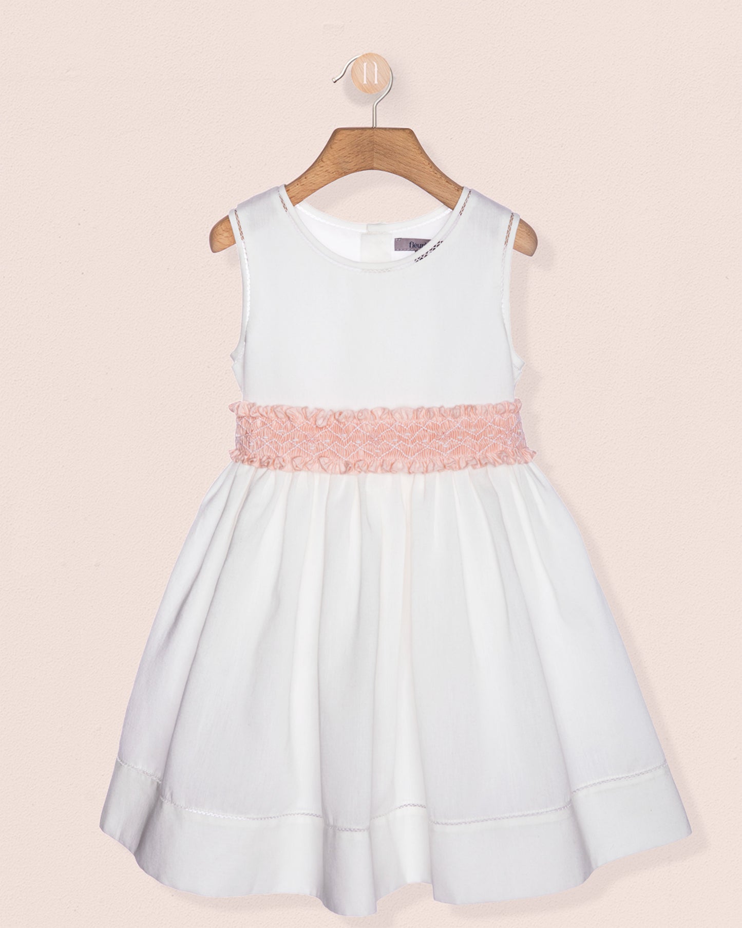 White dress with a pink belt on a hanger against a beige background