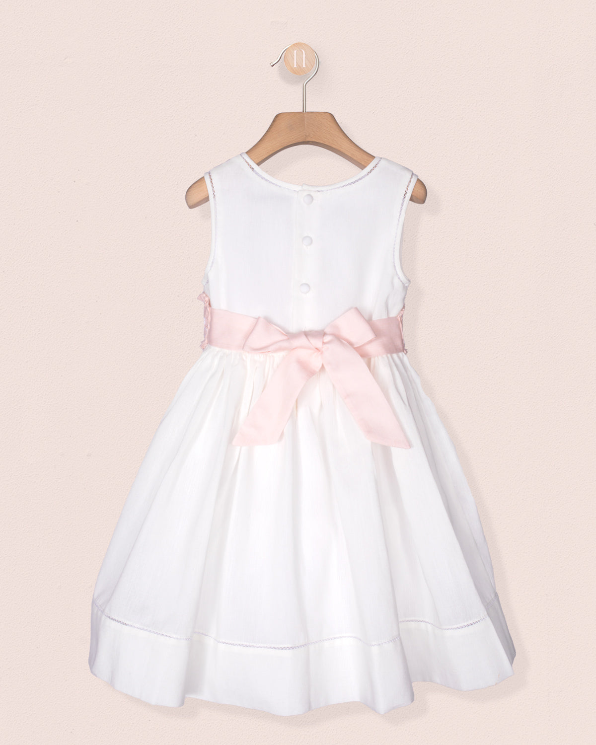 White dress with a pink bow on a beige background