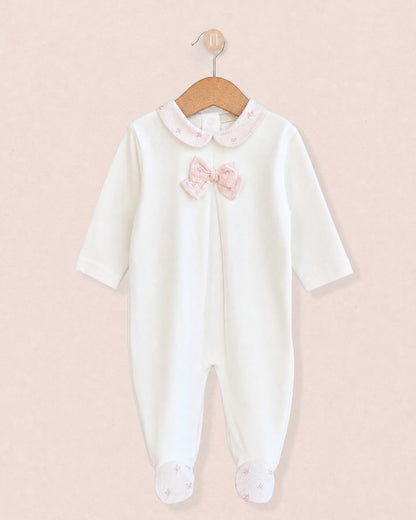 Front of cotton velour baby onesie hanging from wooden hanger, with light pink bows in center of chest, and pink floral motif collars and feet.